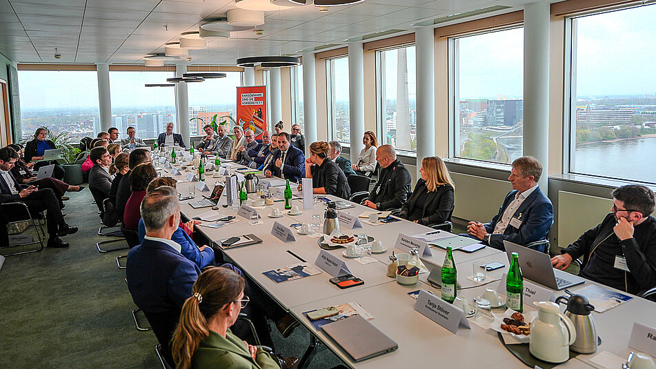 Foto aller Teilnehmenden an langem Tisch mit großen Fenstern im Hintergrund die einen Blick auf Düsseldorf bieten