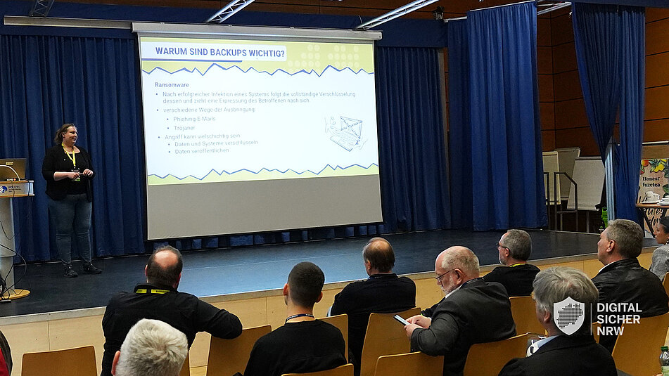 Präsentation einer Referentin auf einer Bühne vor Publikum